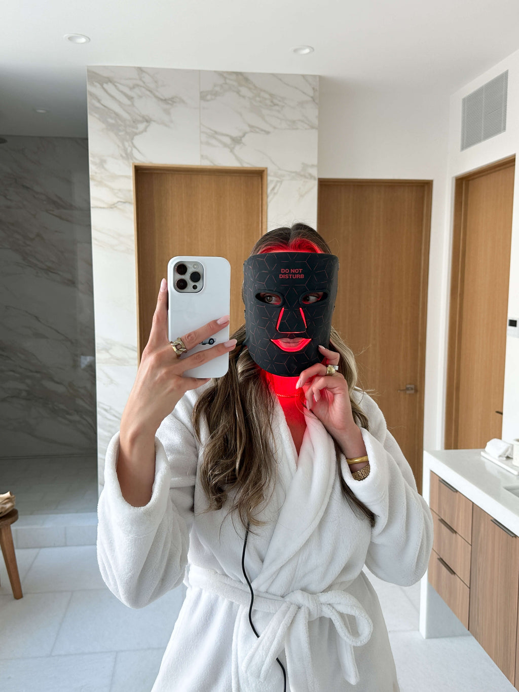 Woman photographing herself while wearing the Renew Red Light Mask