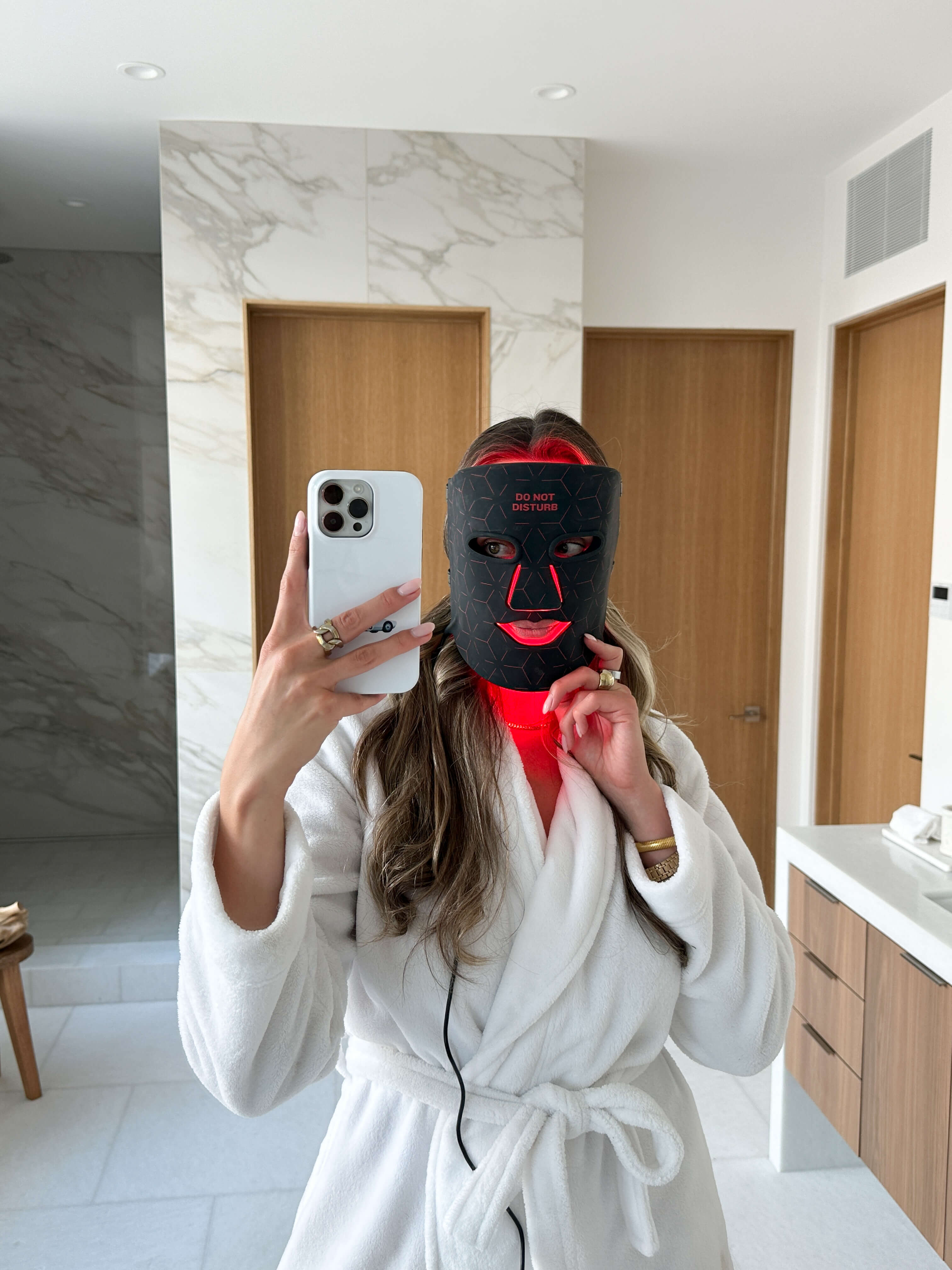 Woman photographing herself while wearing the Renew Red Light Mask